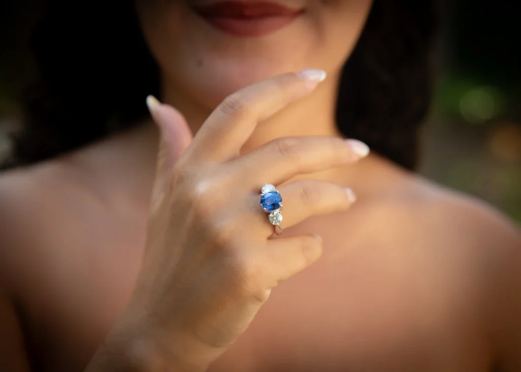 Close-up of a woman wearing a sapphire and diamond three-stone ring on her finger with a softly blurred background.